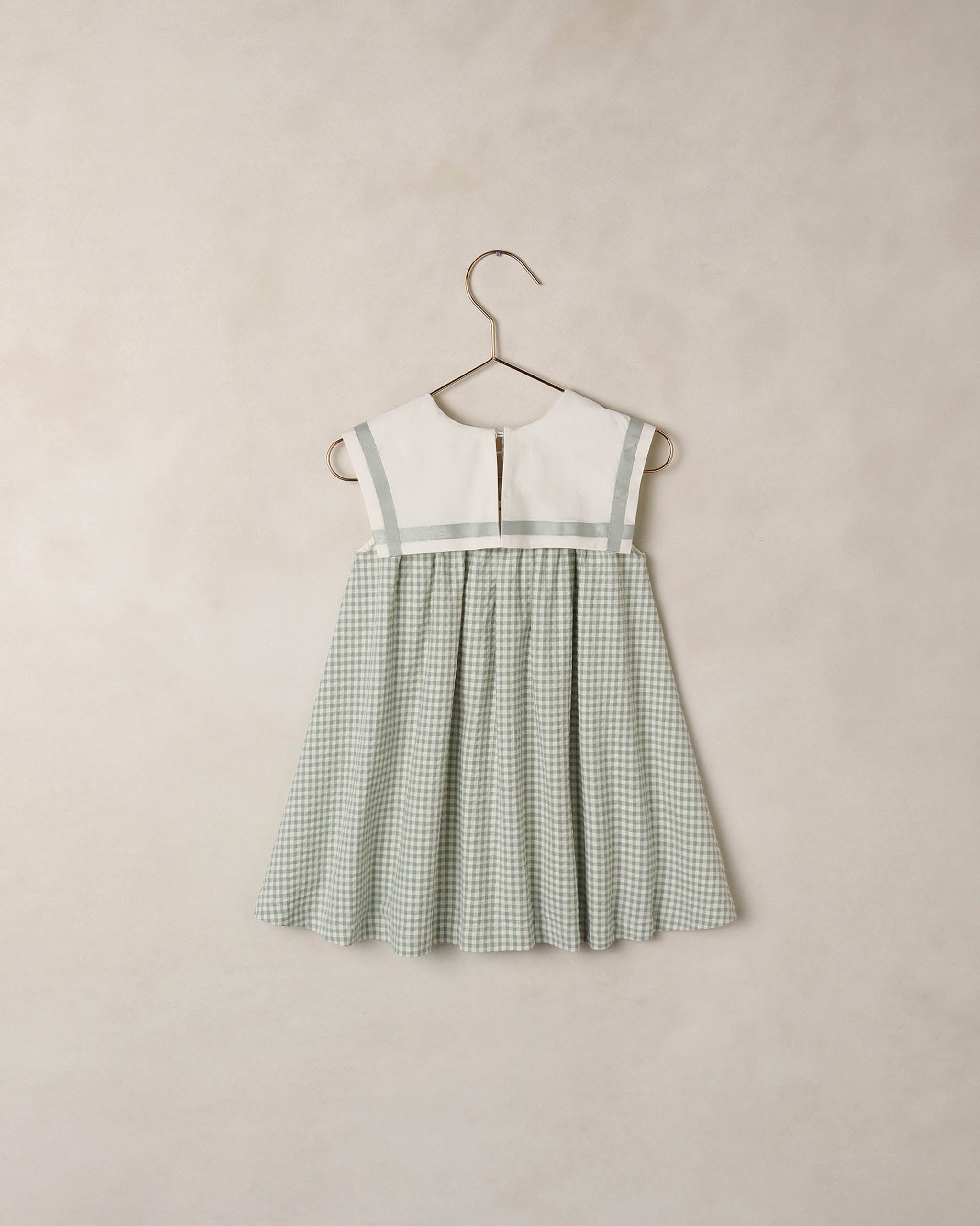 Green checkered dress on a hanger against a beige background