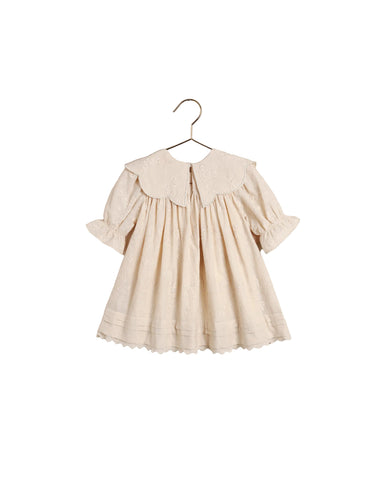 A cream-colored baby dress with a large embroidered Peter Pan collar, short puff sleeves, and a scalloped hem, hanging on a metal hanger against a white backgroundl.
