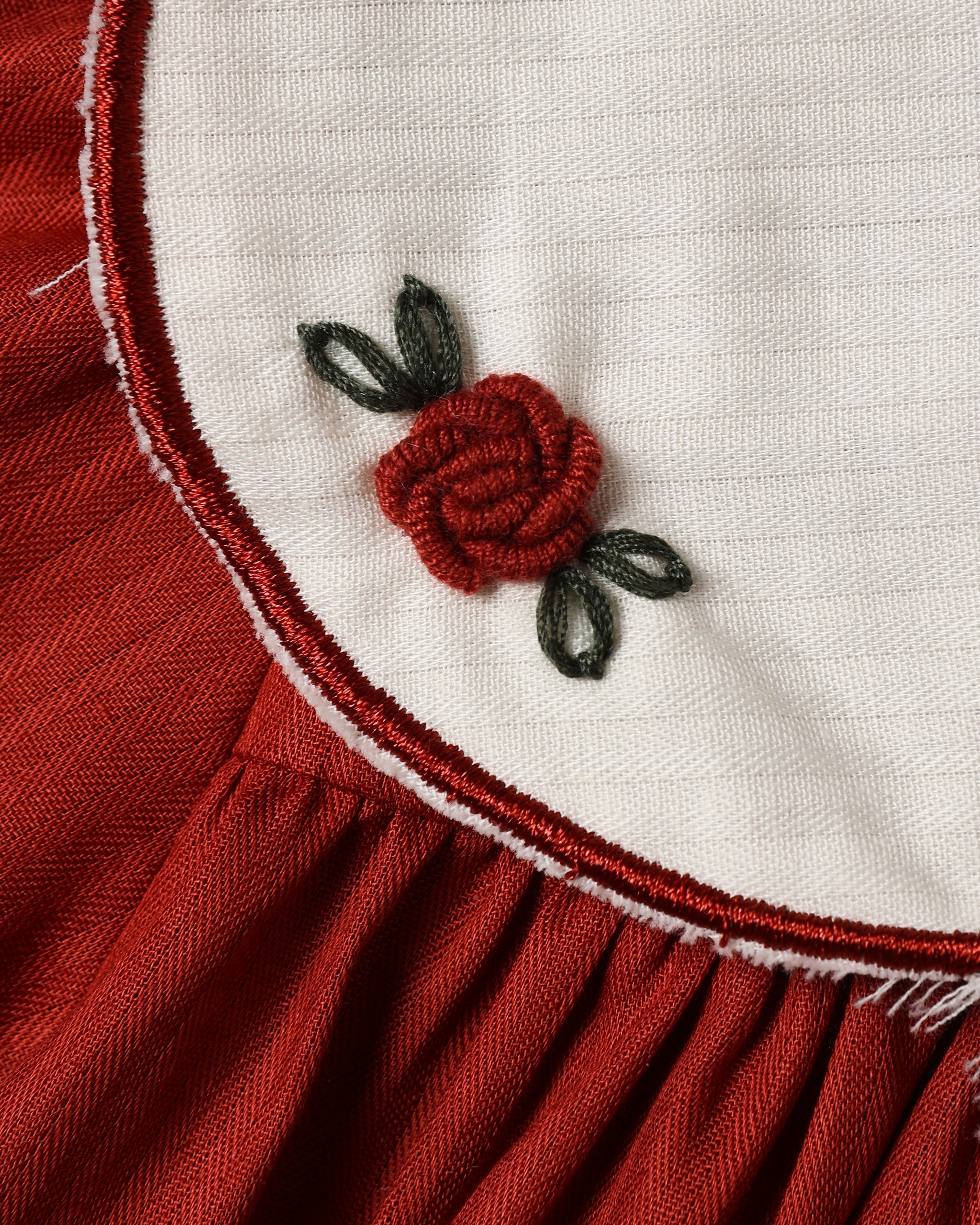 Close up of a Noralee ruby red dress with a cream scalloped collar red trim and delicate embroidered rose detail above the pleated skirt