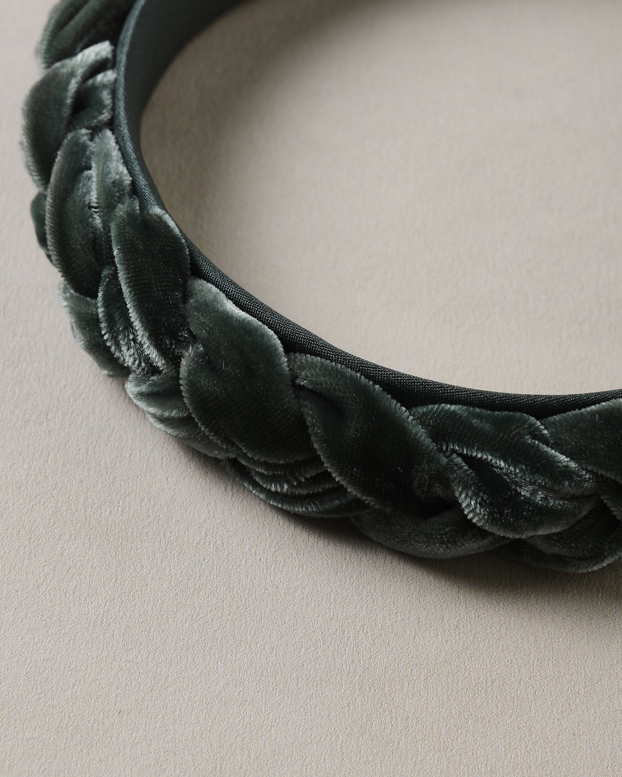 Close up of a deep green braided velvet headband with soft textured loops on a neutral background from Noralee