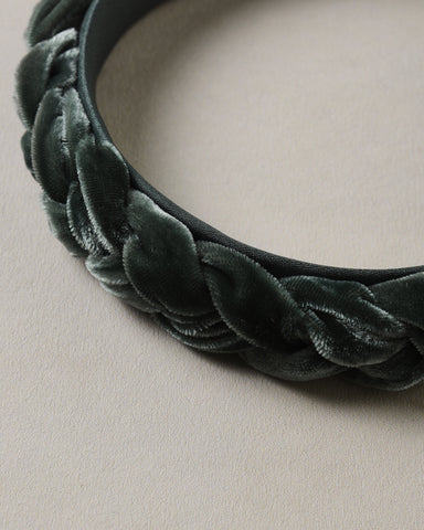 Close up of a deep green braided velvet headband with soft textured loops on a neutral background from Noralee