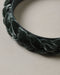 Close up of a deep green braided velvet headband with soft textured loops on a neutral background from Noralee
