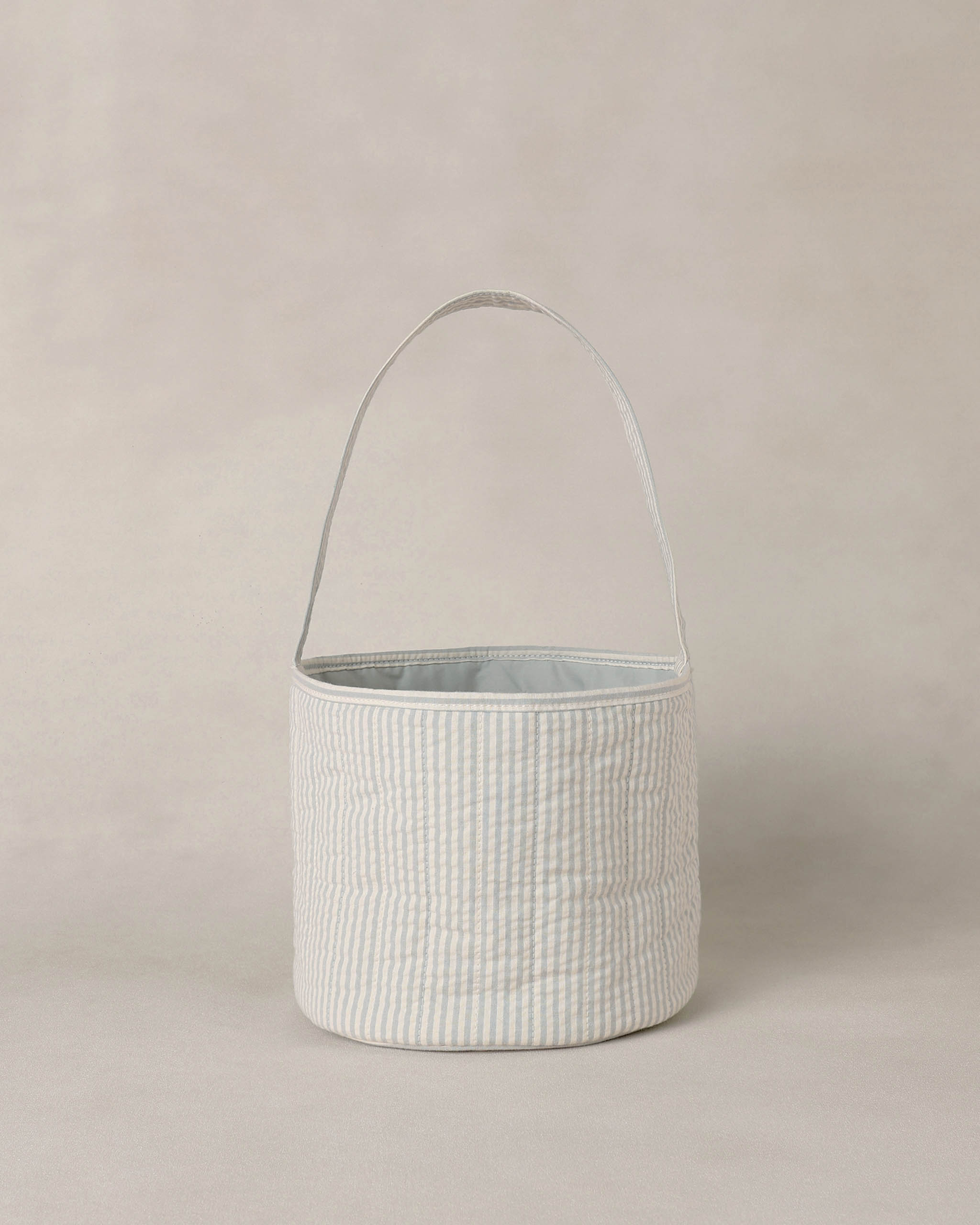 Textured blue and white striped basket with handle on a beige background