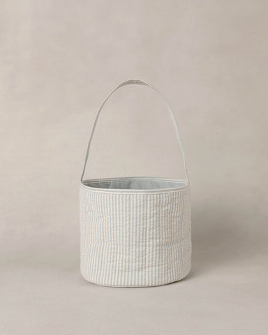 Textured blue and white striped basket with handle on a beige background
