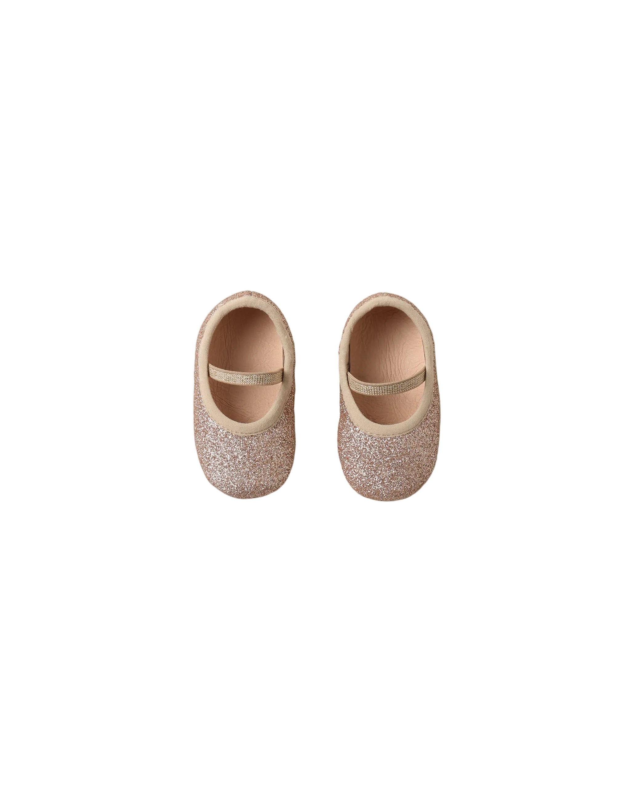 A pair of toddler ballet flats covered in rose gold glitter, featuring a thin metallic glittery strap across the top, shown from a top-down view on a white background.
