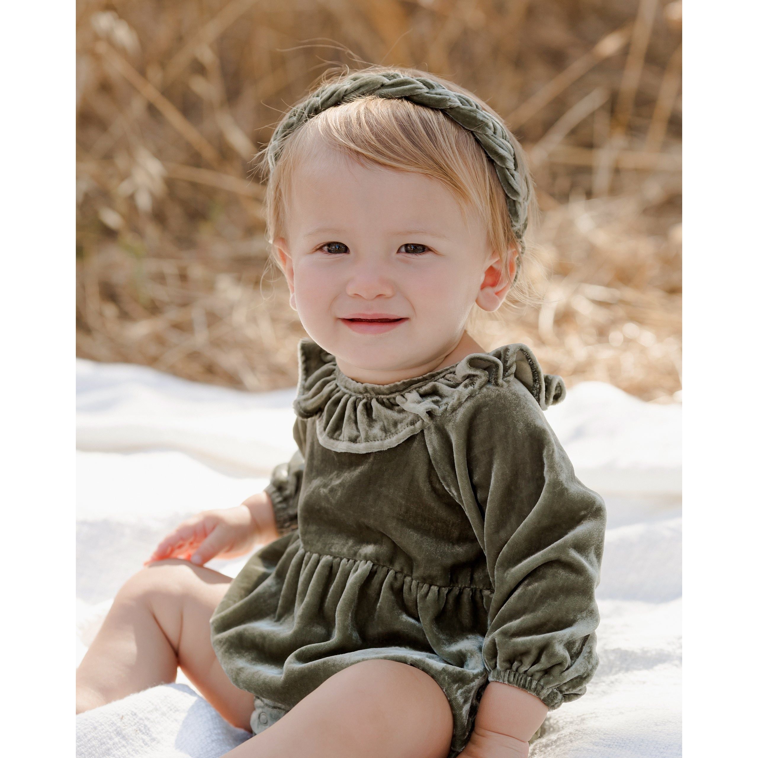 baby girl sitting up wearing pine green colored long sleeve velvet bubble with ruffle detail at the neck and gathered waistline