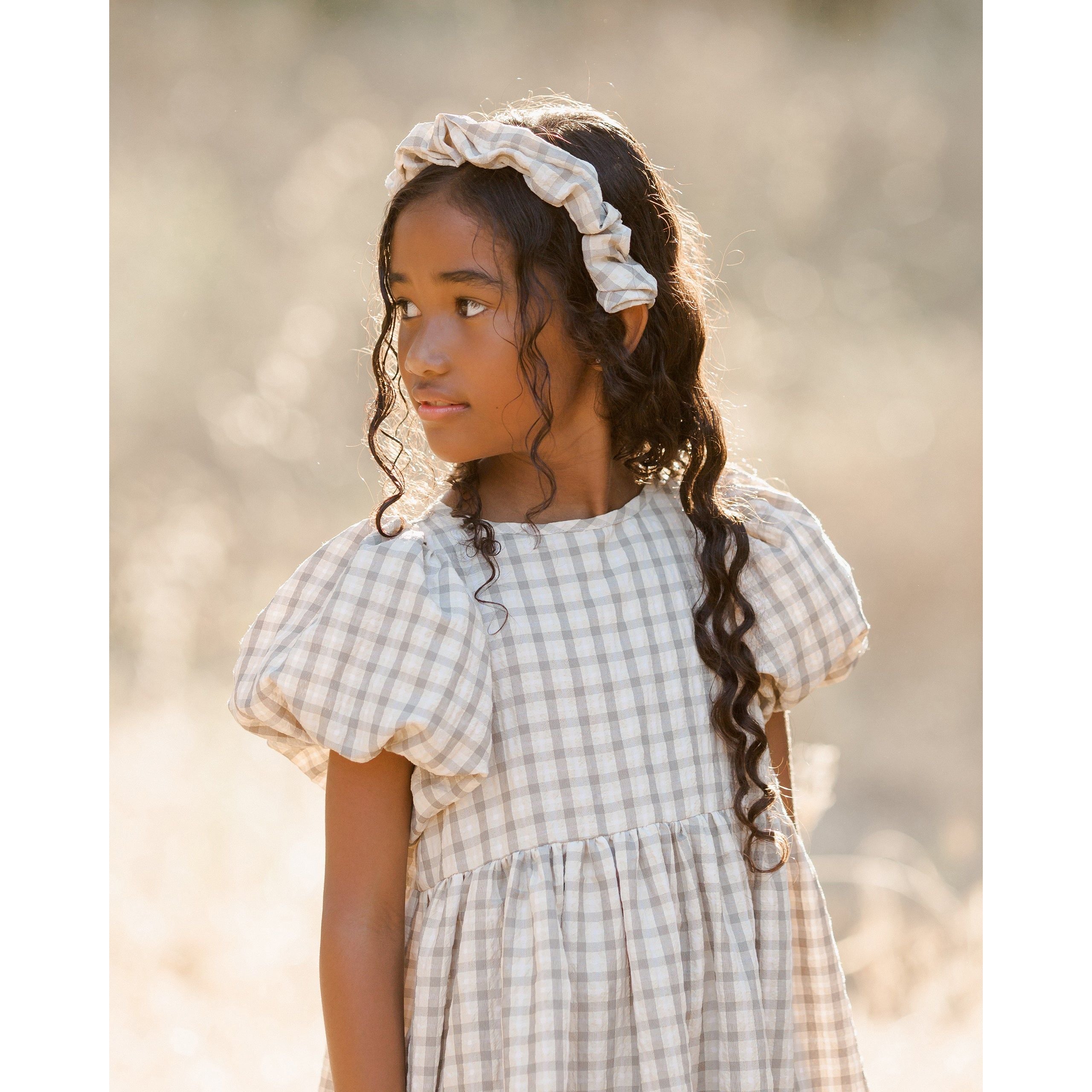 girl wearing girl wearing midi ivory dress with layered tiered skirt, full puffed sleeves, and a delicate button-back closure and green plaid print with matching headband