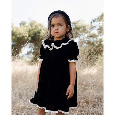 toddler girl wearing black velvet dress with puff sleeves and ruffle at the neck. Lace scallop details on sleeves, ruffles and bottom