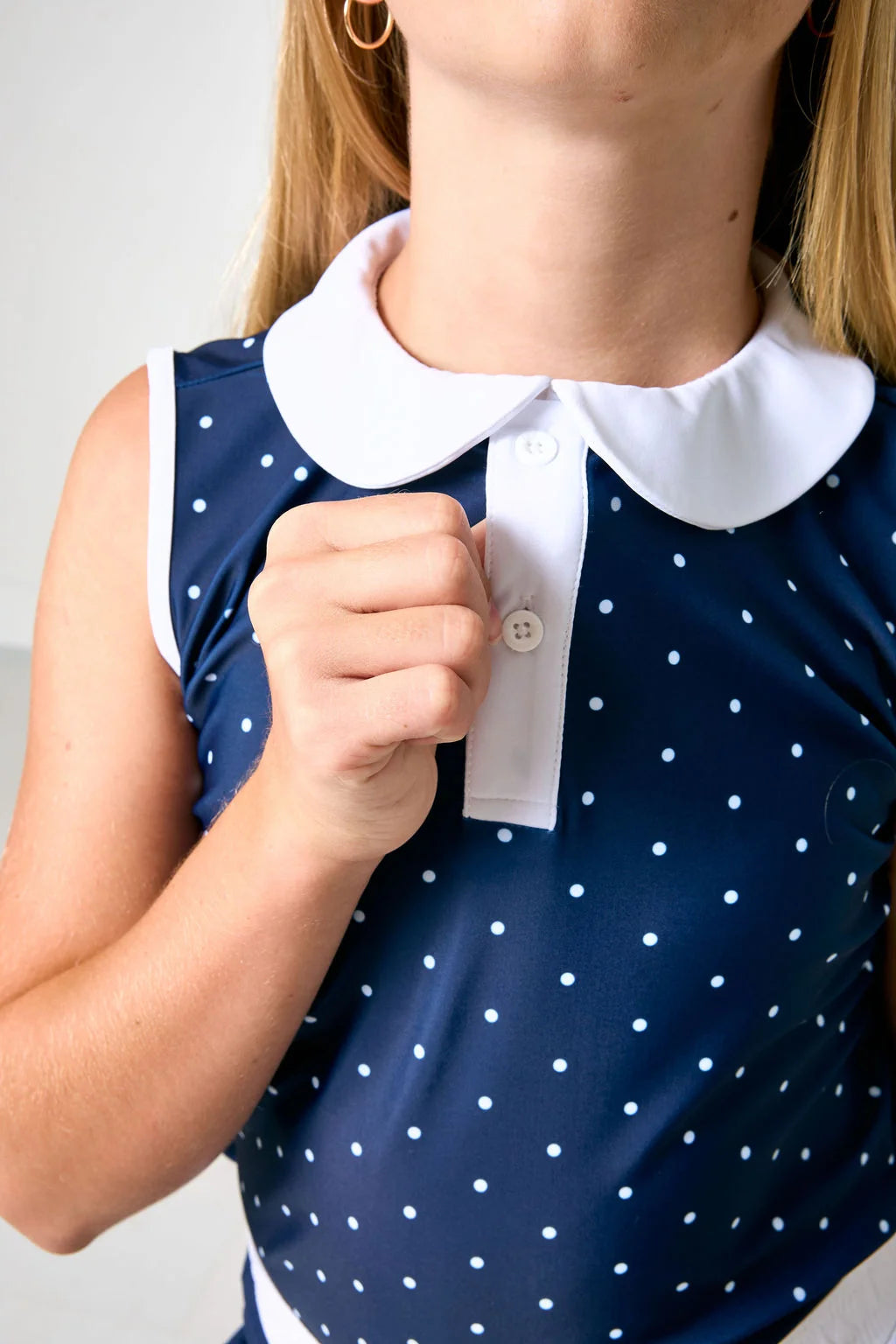 Close-up of a woman wearing a navy blue sleeveless top with white polka dots and a contrasting white Peter Pan collar.
