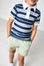 A child wearing a navy blue and white striped short-sleeve polo shirt with a white collar, paired with light green shorts, standing against a plain light gray background.