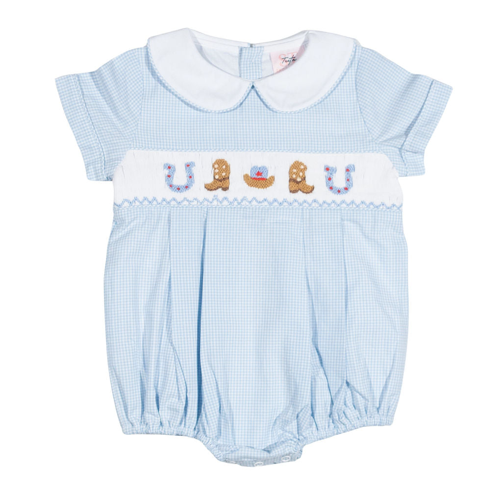 A baby romper in light blue and white gingham with a white Peter Pan collar, featuring a smocked chest band with embroidered cowboy boots, a horseshoe, and a small red heart.