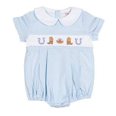 A baby romper in light blue and white gingham with a white Peter Pan collar, featuring a smocked chest band with embroidered cowboy boots, a horseshoe, and a small red heart.