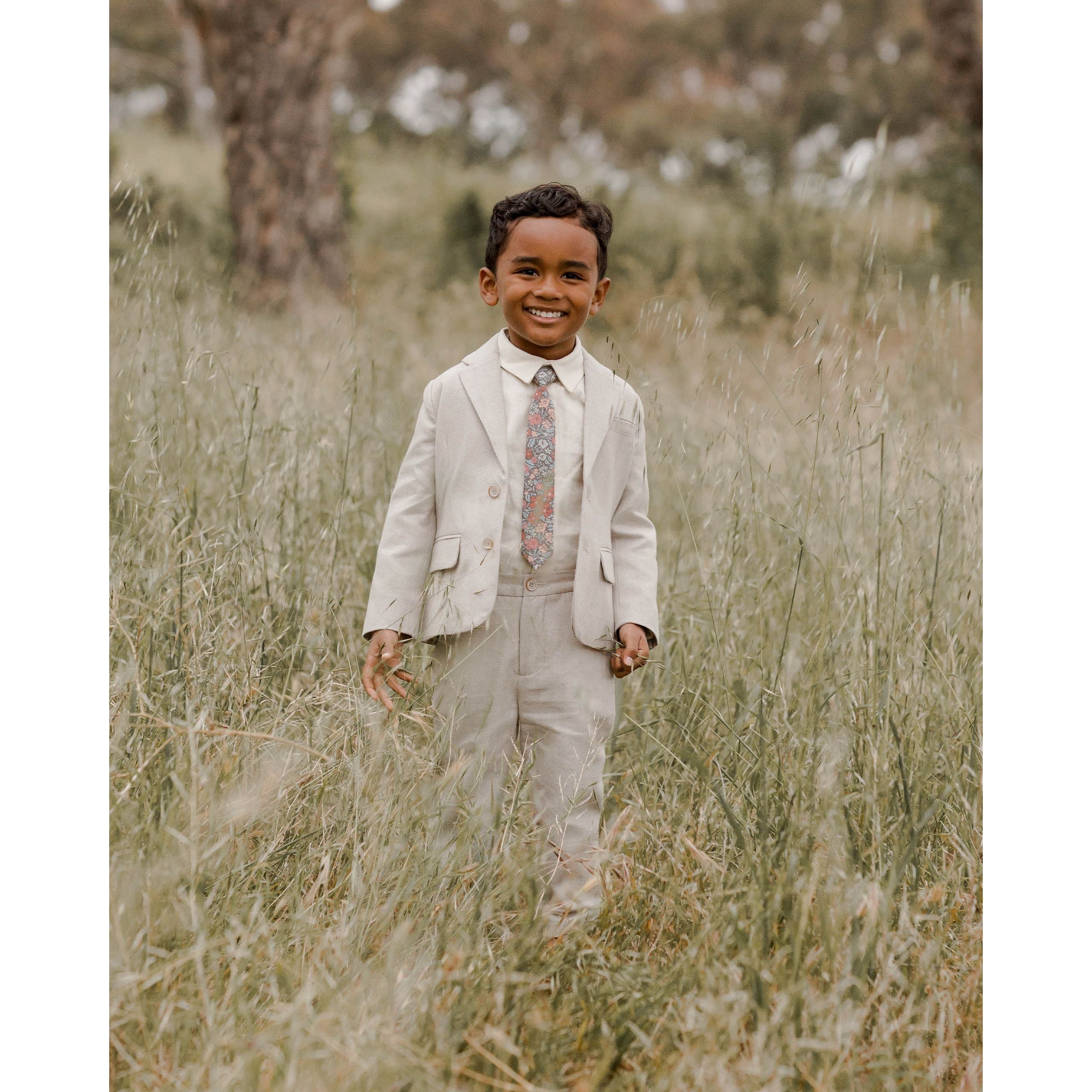 boy wearing navy colored skinny tie with berry garden floral print with linen suit and white button down shirt