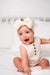 A baby sitting wearing a beige colored cable knit bow headband