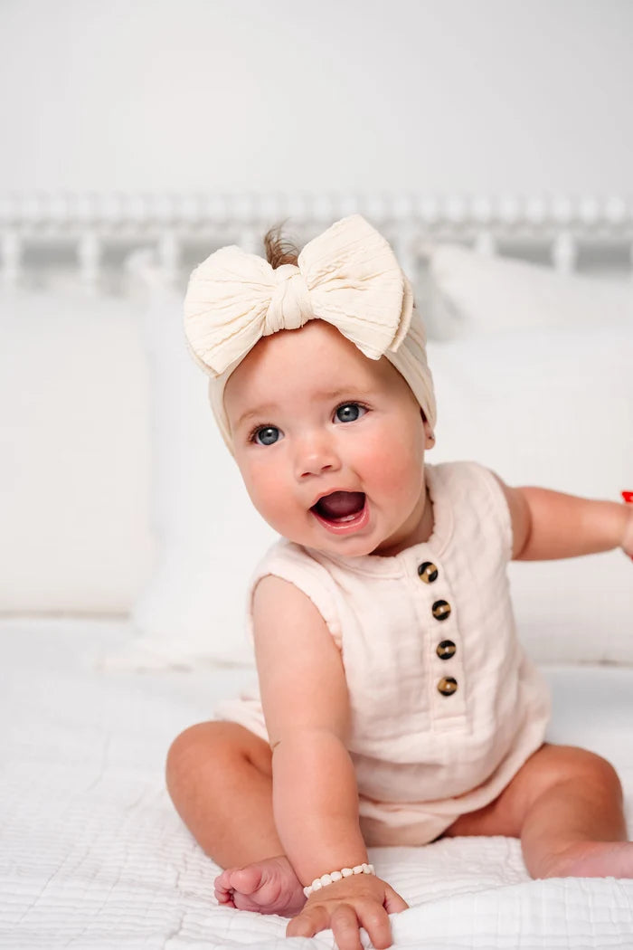 A baby sitting wearing a beige colored cable knit bow headband