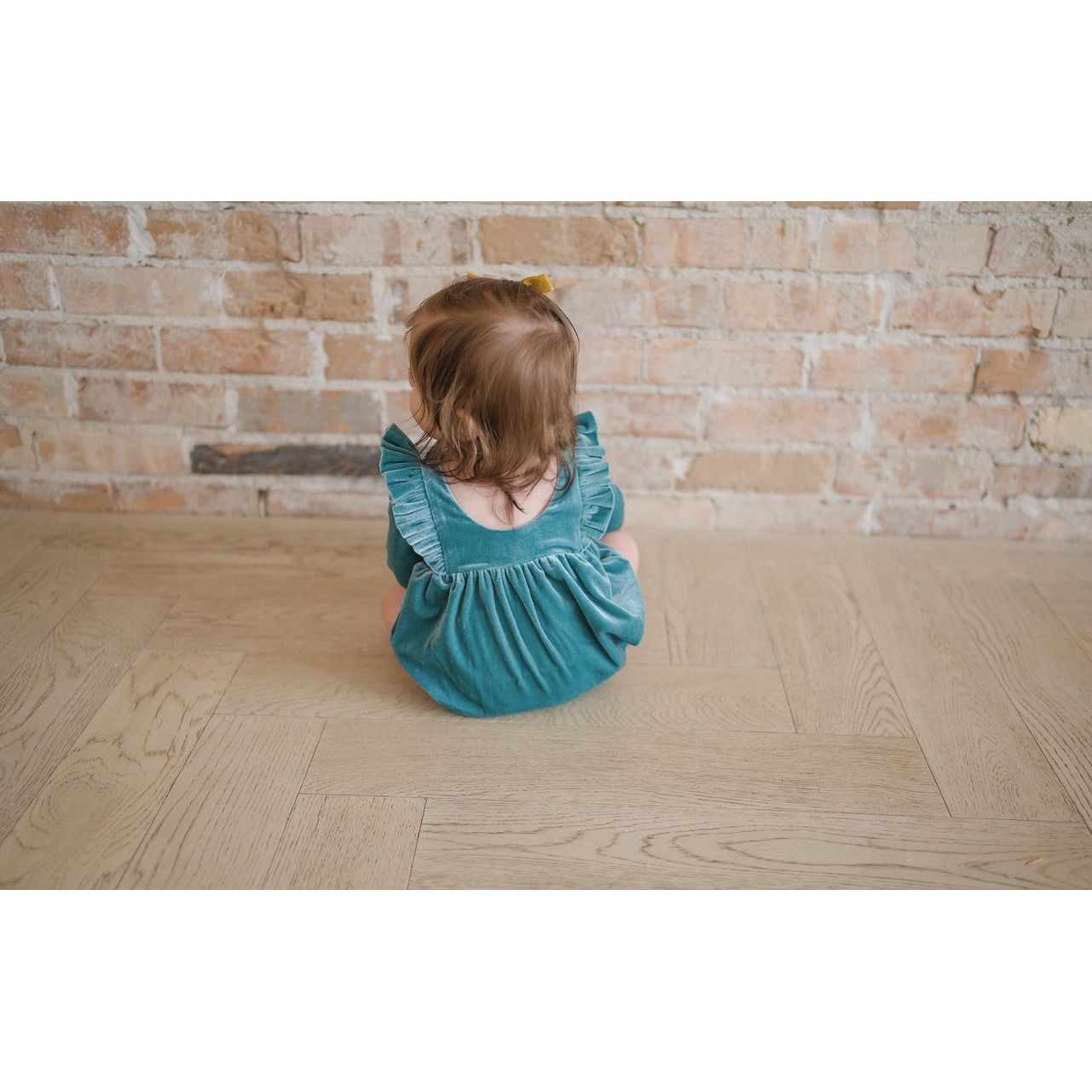back of toddler girl wearing blue/green velvet long sleeve bubble romper with ruffle detail in front and back