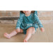 close up view of toddler girl wearing blue/green velvet long sleeve bubble romper with ruffle detail in front and back