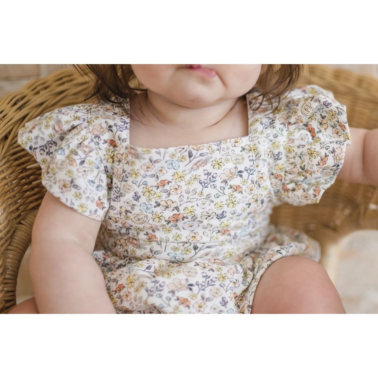 up close view of baby girl wearing white ruffle sleeve bubble with floral print