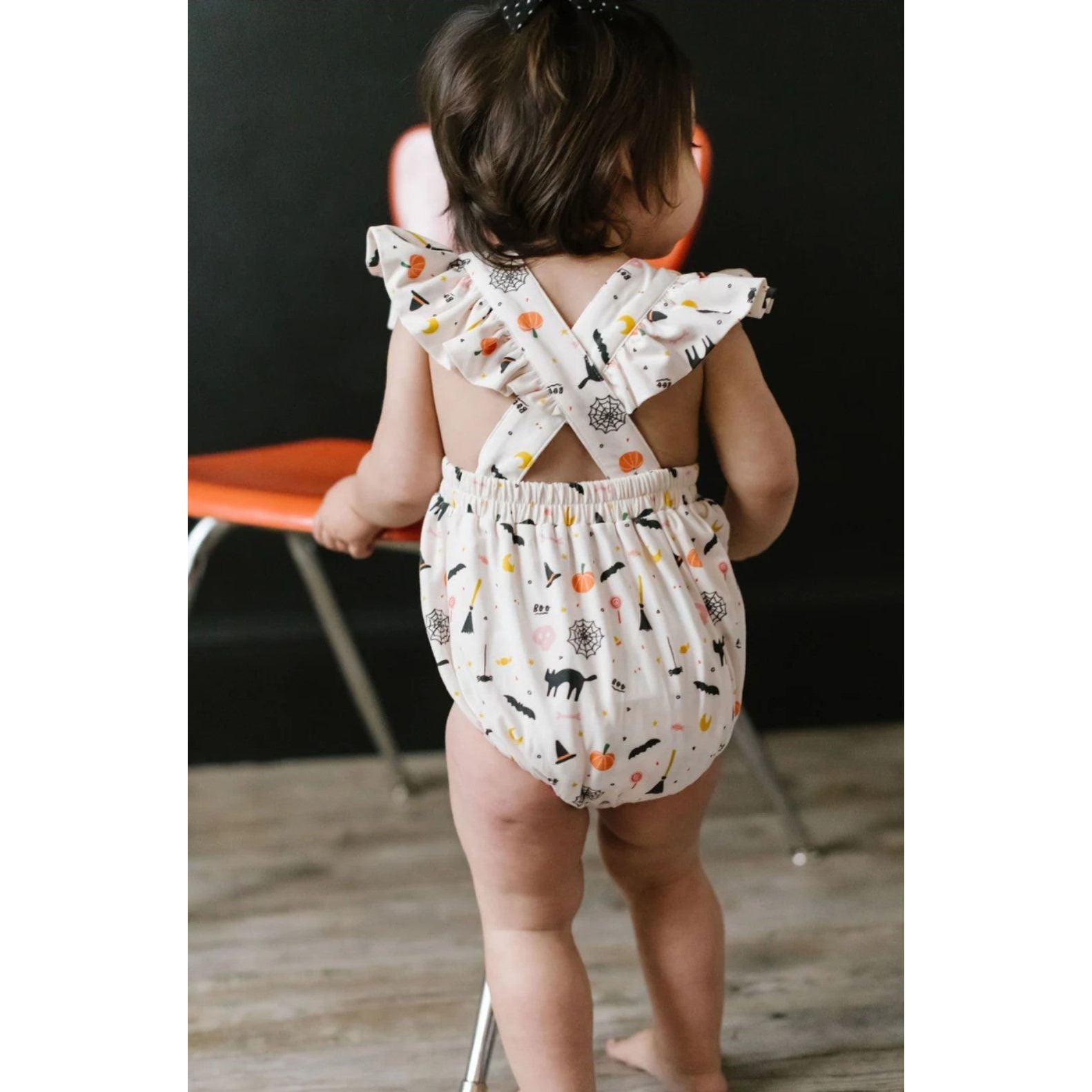 back view of toddler girl wearing white ruffle short sleeved bubble romper with spooky scenes print with criss cross detail in back