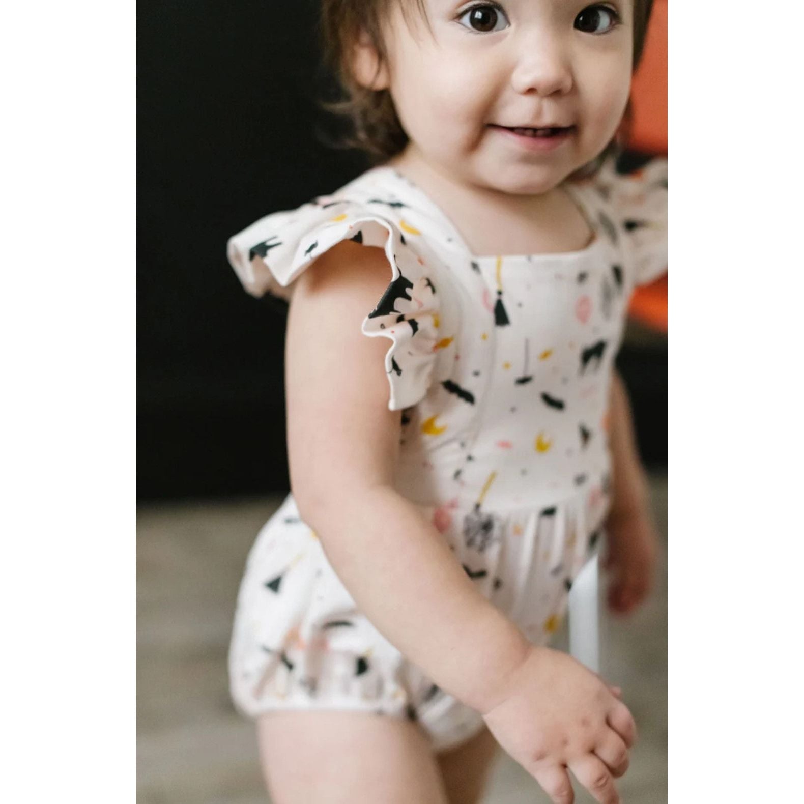 toddler girl wearing white ruffle short sleeved bubble romper with spooky scenes print