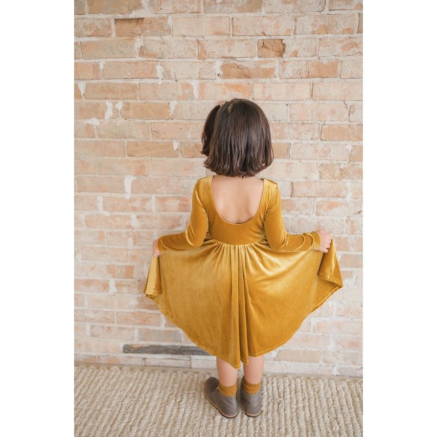 back of girl wearing long sleeve golden yellow velvet twirl dress with scoop back detail