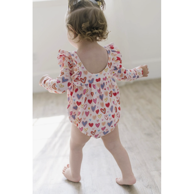 back of baby girl wearing white long sleeve ruffled bubble romper with multicolored hearts print