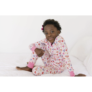 girl wearing white long sleeve loungewear set with multicolored hearts print and pink cuffs at the wrist and ankles