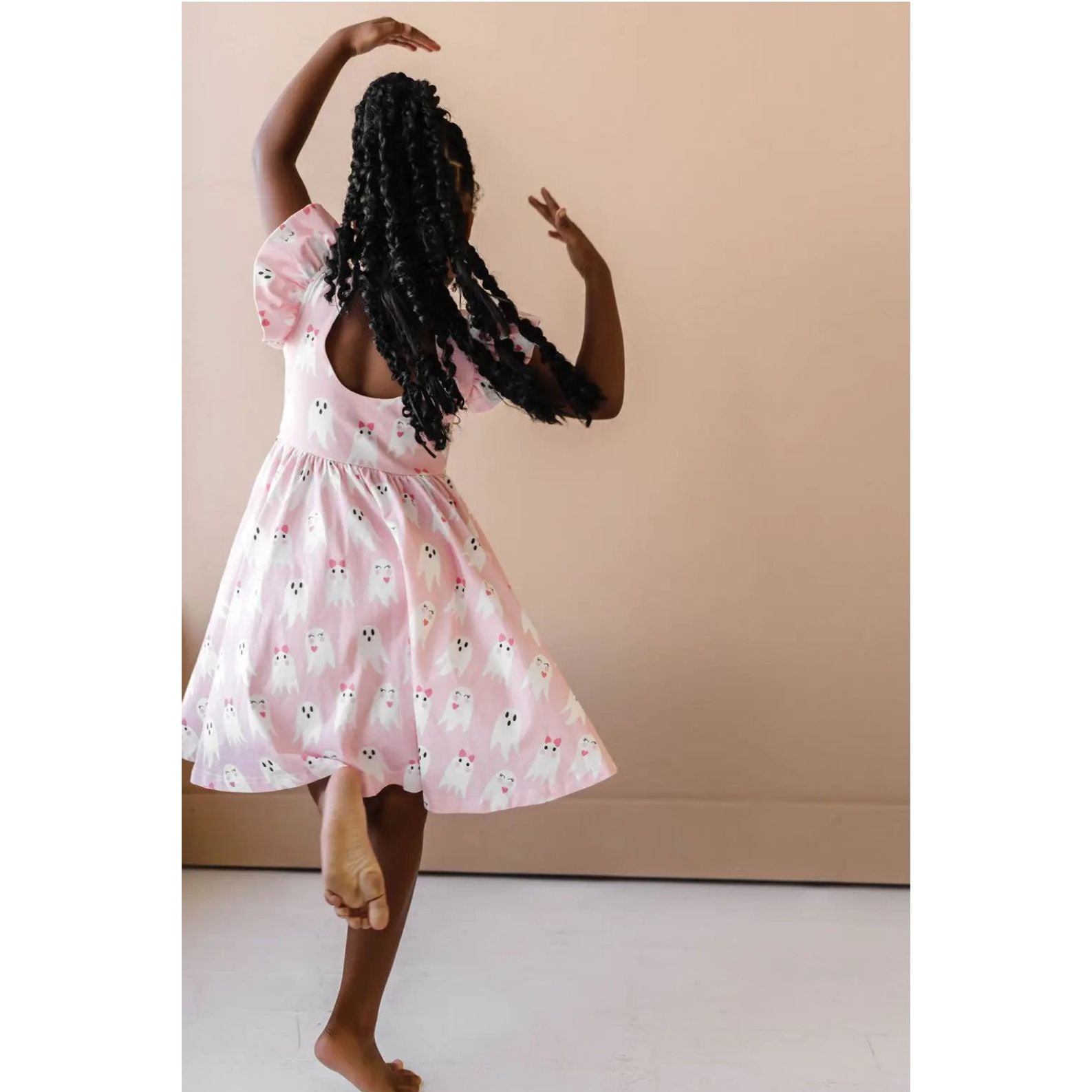 back view of girl twirling in pink ruffle short sleeve dress with girly ghost print with scoop back detail