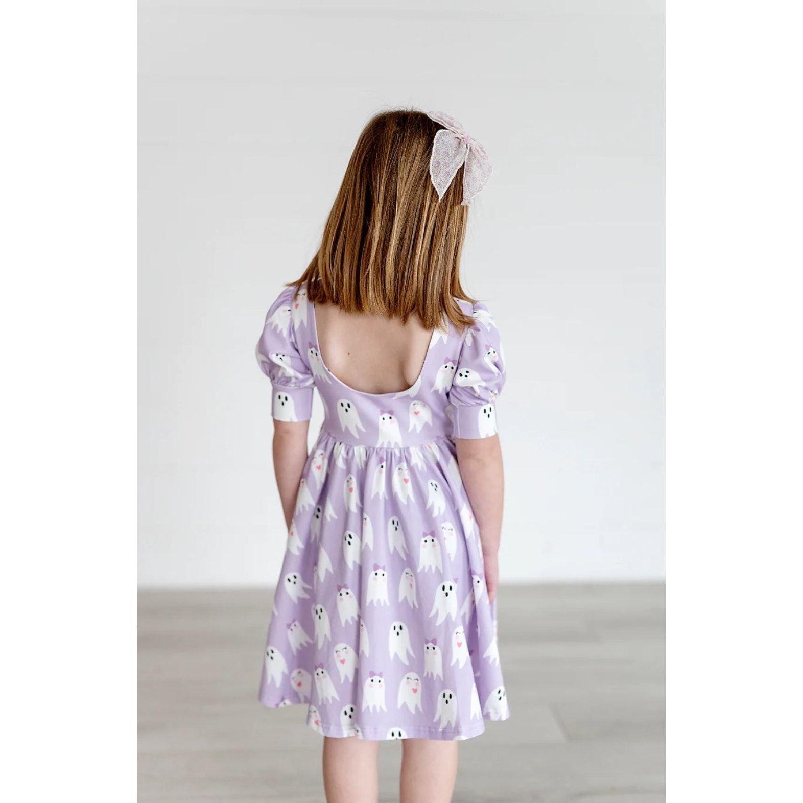 back of girl wearing purple dress with puff short sleeves and scoop back in girly ghost pattern 
