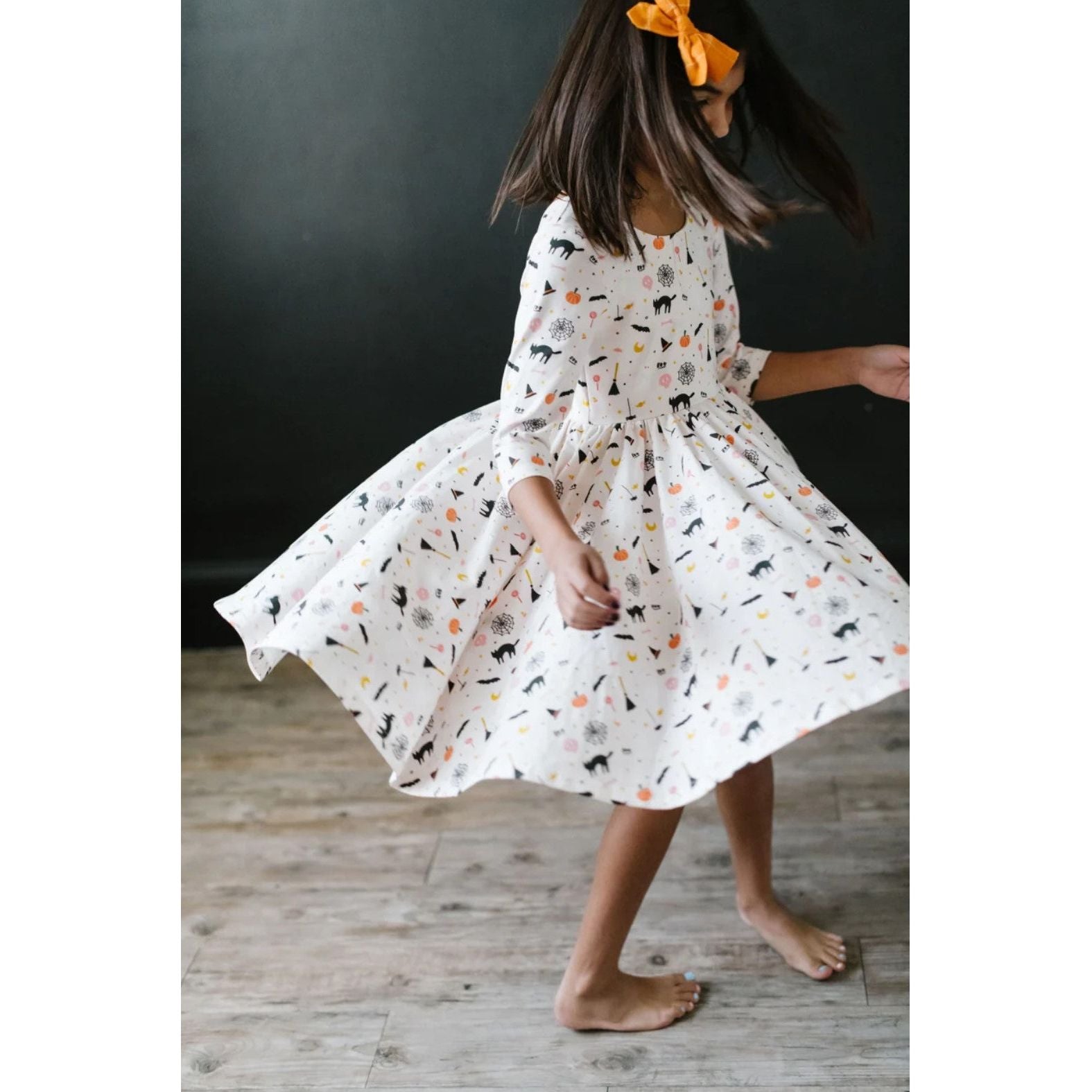 girl twirling in 3/4 length sleeve white dress with spooky scenes print
