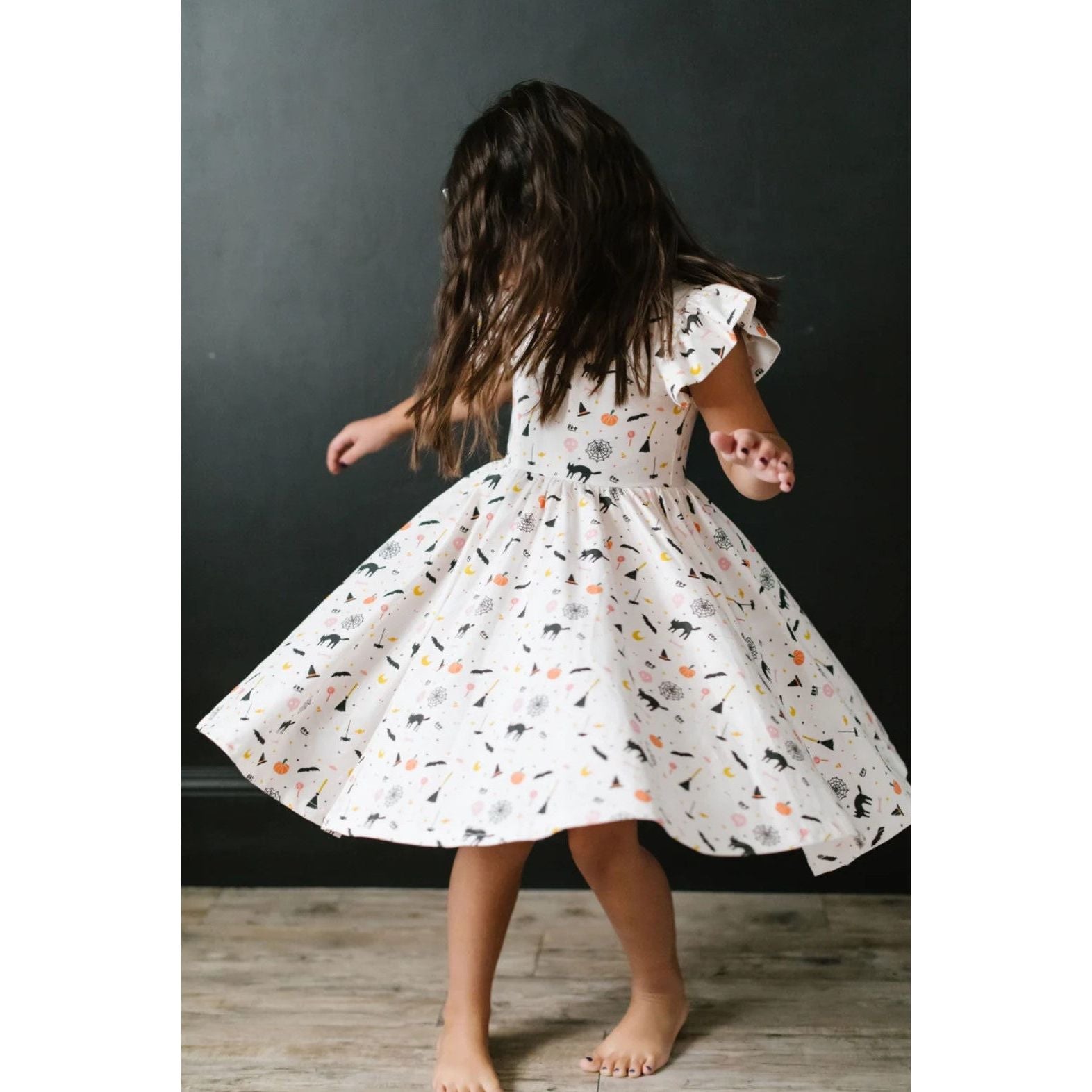 girl twirling in white ruffle short sleeved dress with spooky scenes print