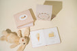 Children's book with illustrations of a teddy bear, ice cream cone, and cake on a beige surface.