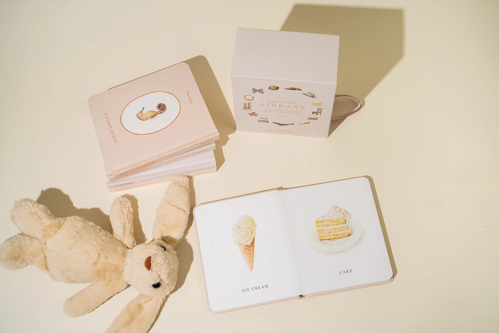 Children's book with illustrations of a teddy bear, ice cream cone, and cake on a beige surface.