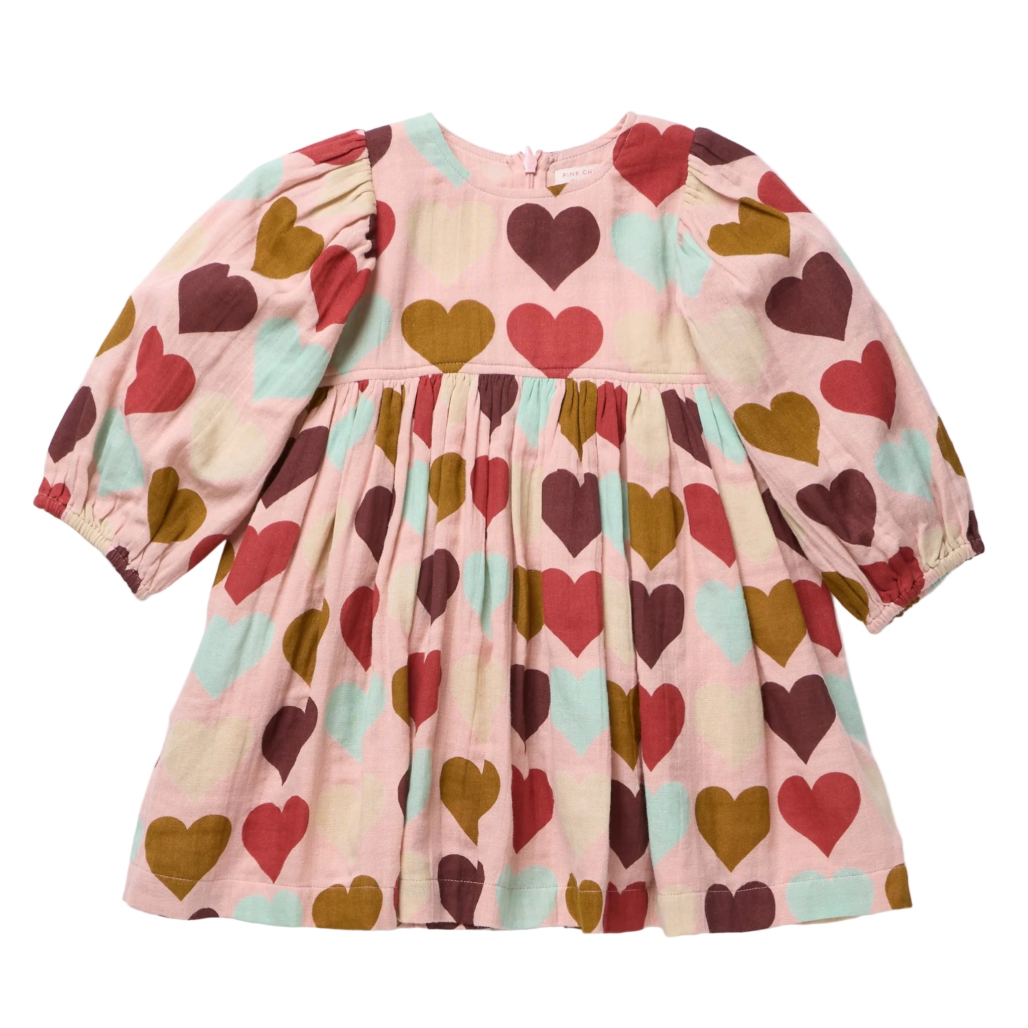A children's long-sleeve dress with a gathered waist and an allover heart print on a light pink base, featuring red, brown, and mint green hearts. The dress is laid flat against a clean white background.