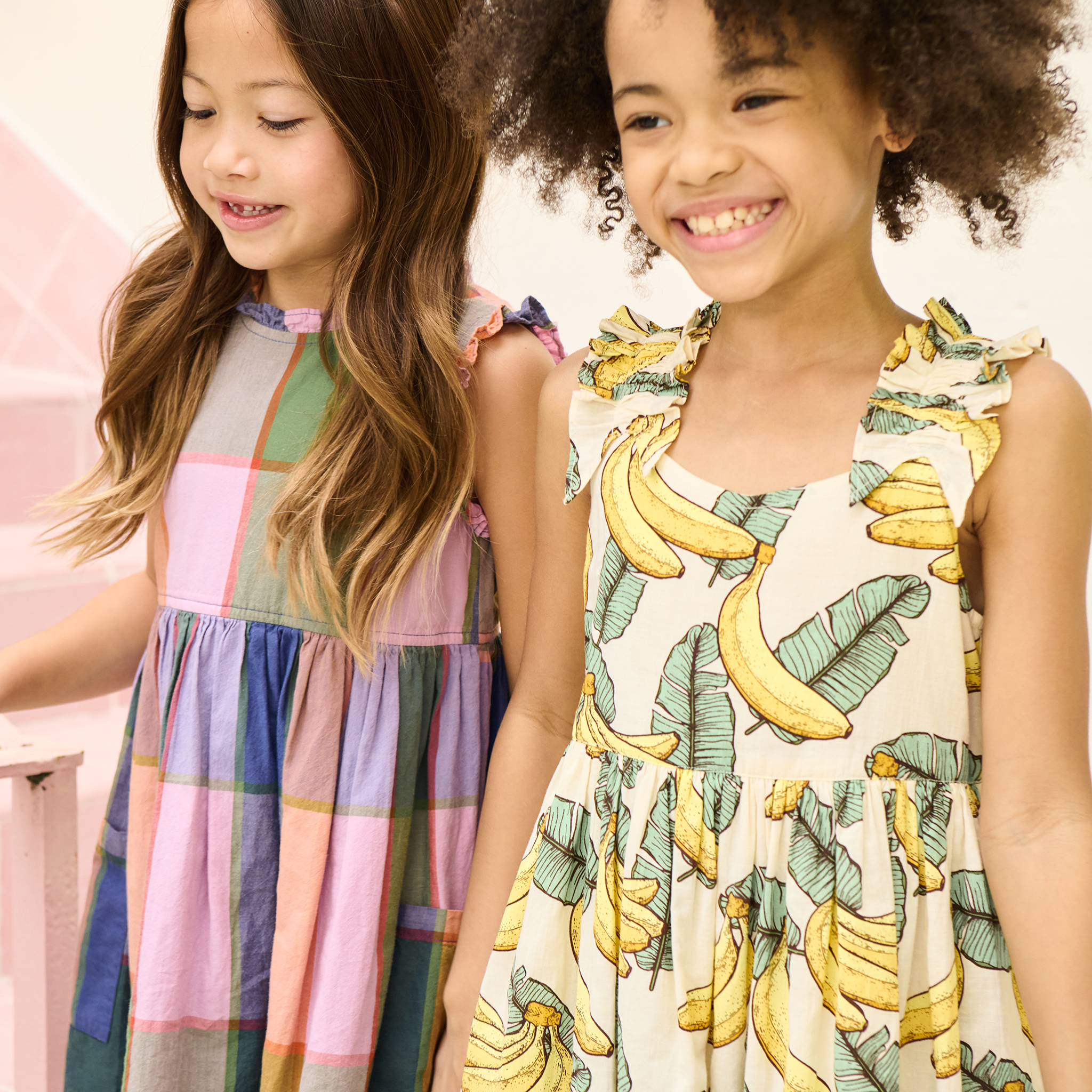 Two young girls wearing colorful dresses, one with a banana pattern, against a light background.
