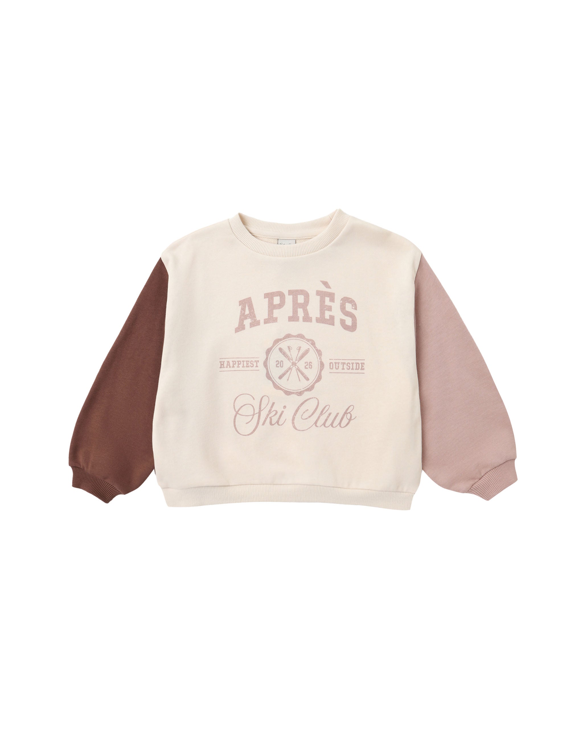 A children's long-sleeve sweatshirt with a cream body, dusty pink sleeves, and a brown sleeve on the left side. The front features a dusty pink graphic reading 'APRÈS Ski Club' with a cross-ski design.