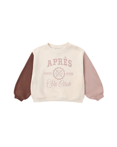 A children's long-sleeve sweatshirt with a cream body, dusty pink sleeves, and a brown sleeve on the left side. The front features a dusty pink graphic reading 'APRÈS Ski Club' with a cross-ski design.
