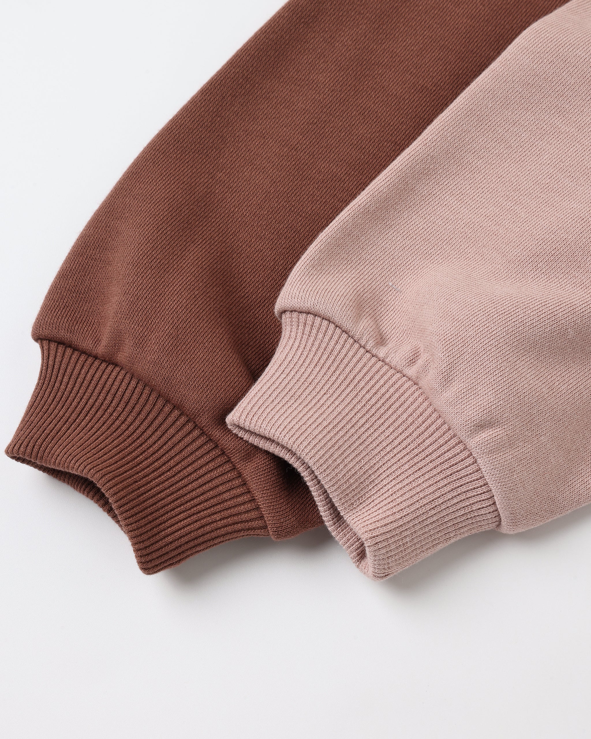 Close-up of two ribbed knit sleeve cuffs in warm brown and dusty pink, laid diagonally on a clean white background.
