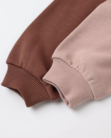 Close-up of two ribbed knit sleeve cuffs in warm brown and dusty pink, laid diagonally on a clean white background.