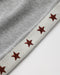 Close-up detail of a light gray knit fabric with a cream-colored trim featuring embroidered red stars.