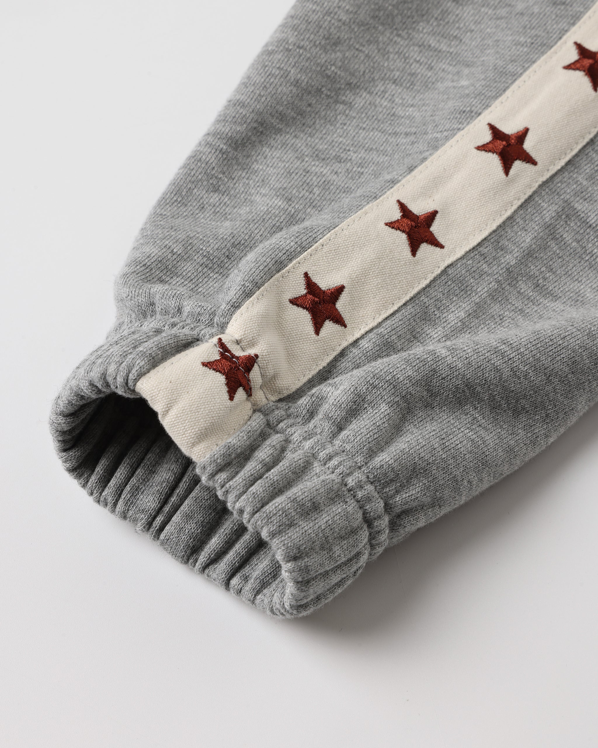 Close-up of a gray ribbed knit garment cuff with a cream fabric stripe running along the side, decorated with embroidered metallic red stars.
