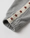 Close-up of a gray ribbed knit garment cuff with a cream fabric stripe running along the side, decorated with embroidered metallic red stars.