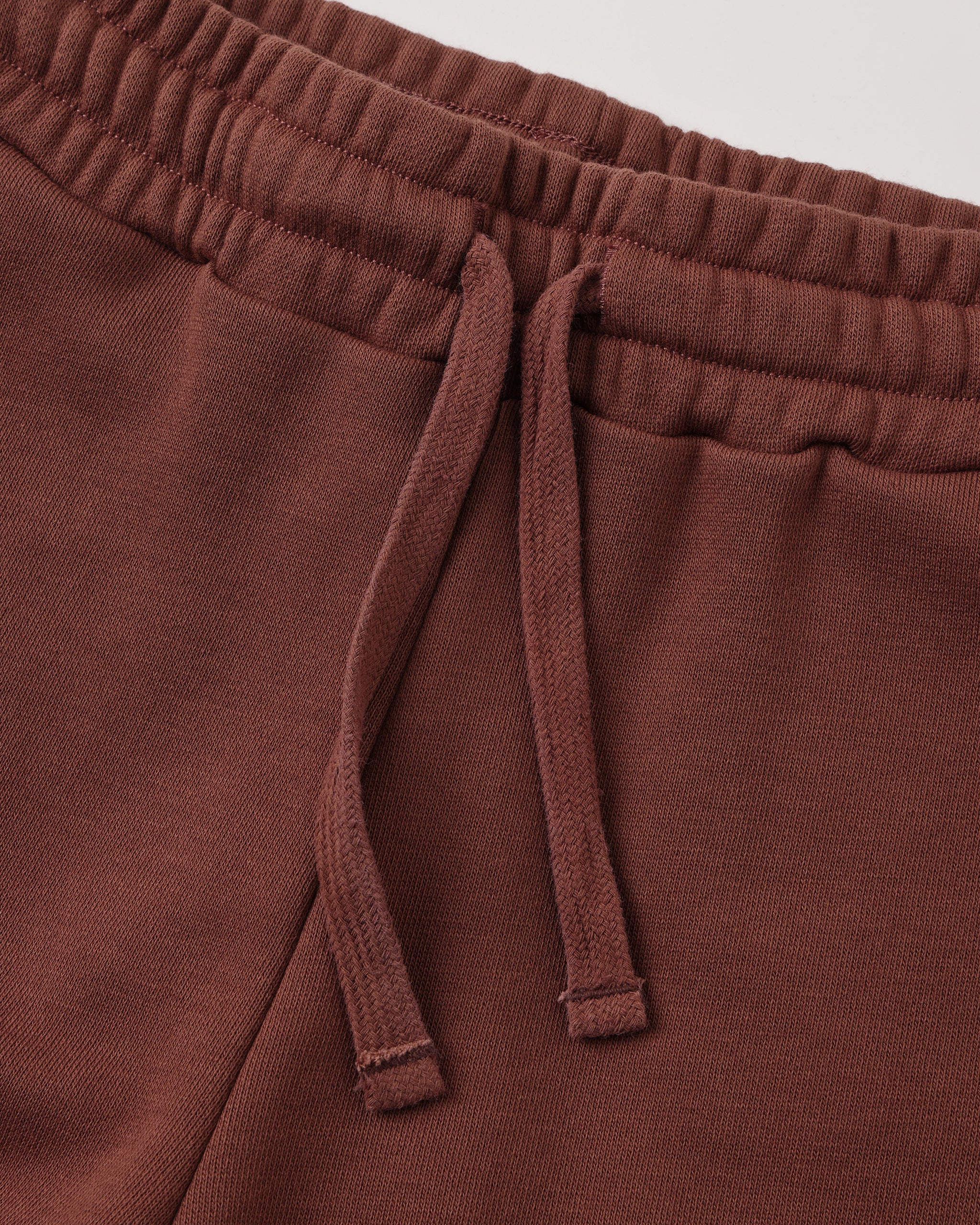 Close-up of a pair of brown sweatpants showing the elastic waistband and matching drawstring.