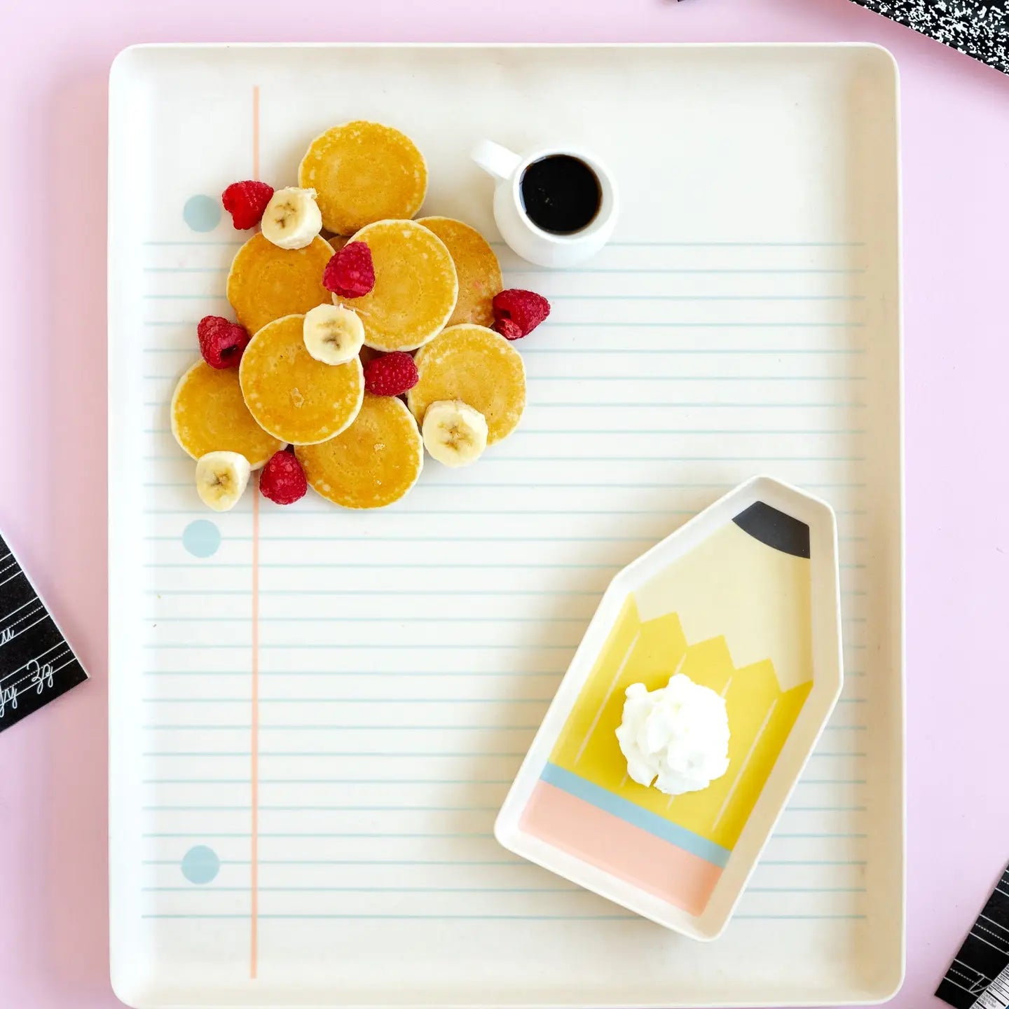 Plated dessert with pancakes, fruit, and a small cup on a pink surface