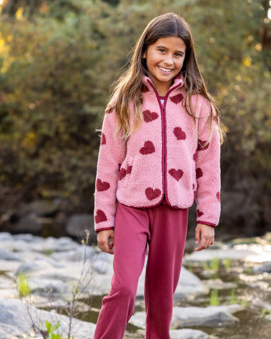 A girl next to a stream wearing a pink jacket with dark pink hearts pattern