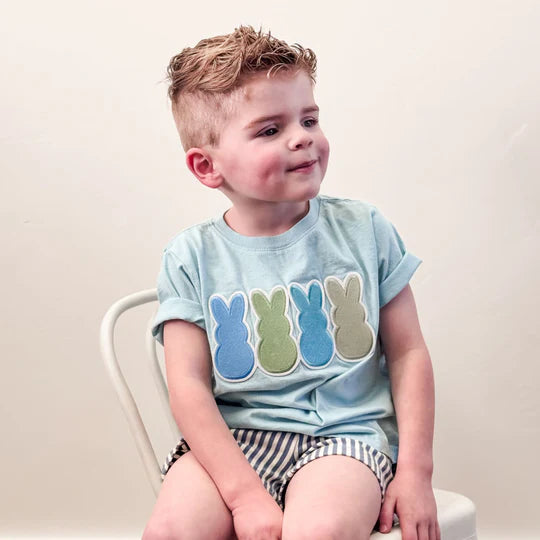 Child wearing a light blue t-shirt with colorful bunny designs, sitting on a white chair.