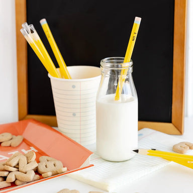 Glass bottle of milk with a yellow pencil, cup with more pencils, and cookies on a table.