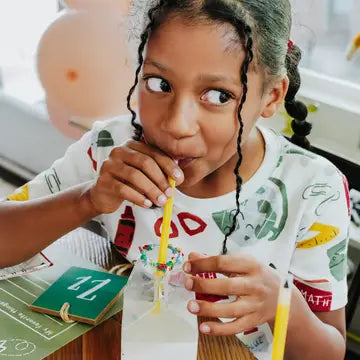 Child drinking from a straw with a colorful shirt and balloons in the background