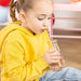 Child in a yellow hoodie drinking from a glass with a straw indoors.