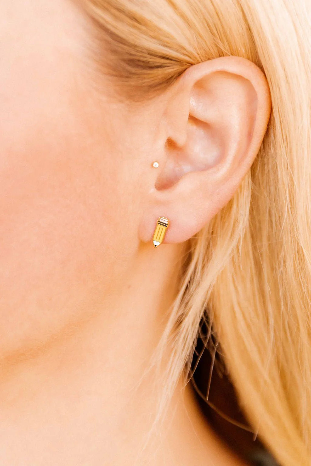 Close-up of an ear wearing a pencil earring with blonde hair.